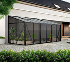 Modern garden room with glass walls and plants, attached to a house.