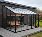 A modern black metal patio sunroom with glass panels on a gray deck, featuring a hanging wooden swing with a tan canopy in front, set against a dark wood house exterior.
