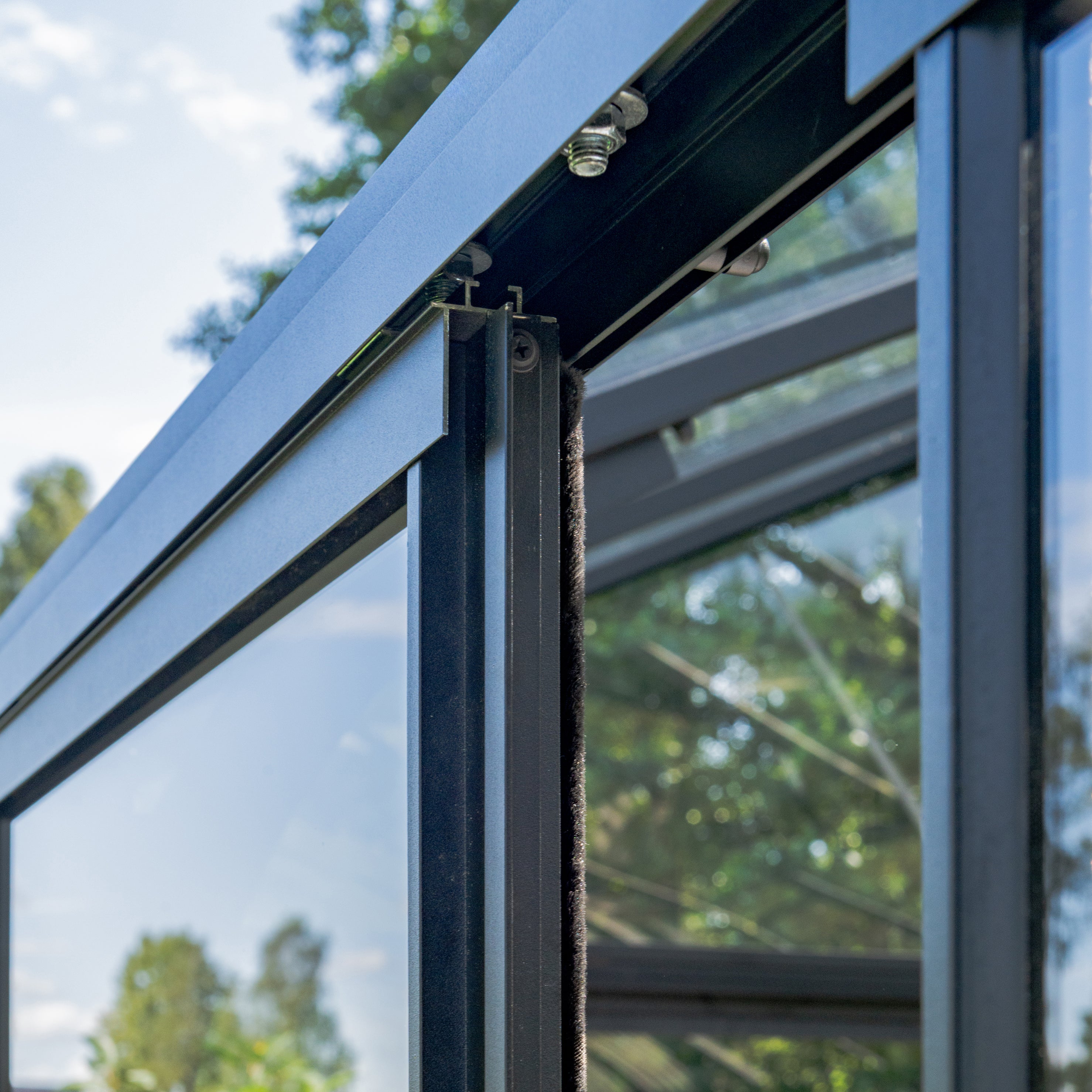 Close-up of a glass door with a weather stripping detail, showing trees in the background.
