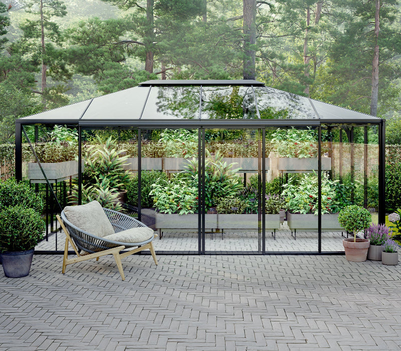 Hexagonal glass gazebo with a chair on a paved patio surrounded by greenery