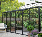 Greenhouse with glass walls and a patio area featuring chairs and plants.