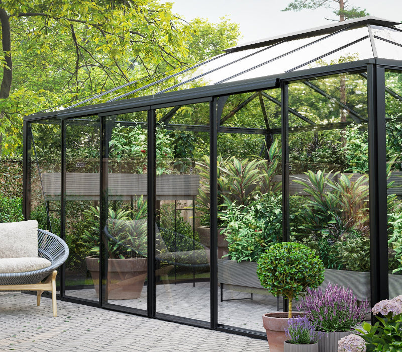 Greenhouse with glass walls and a patio area featuring chairs and plants.