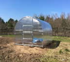 Silver greenhouse on a grassy field with trees in the background